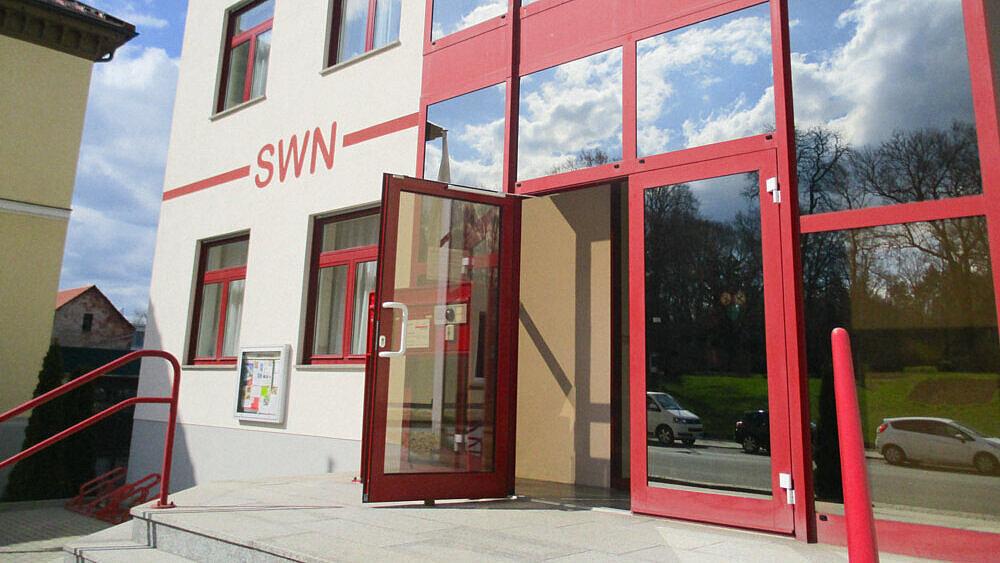 Offene Eingangstür des SWN-Gebäudes zur Ernst-Thälmann-Straße im Sonnenlicht